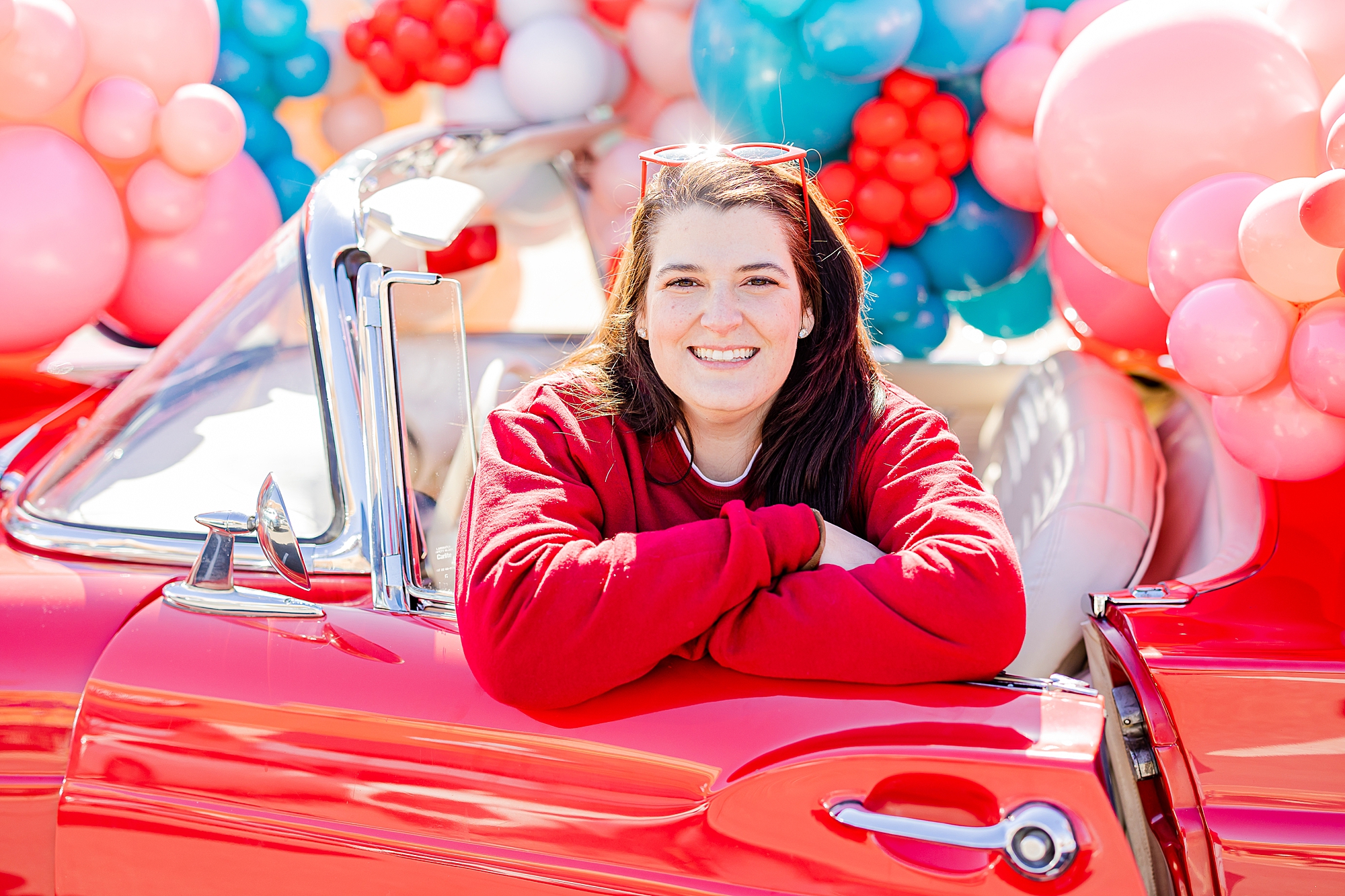 woman in red water smiles leaning against side of red car